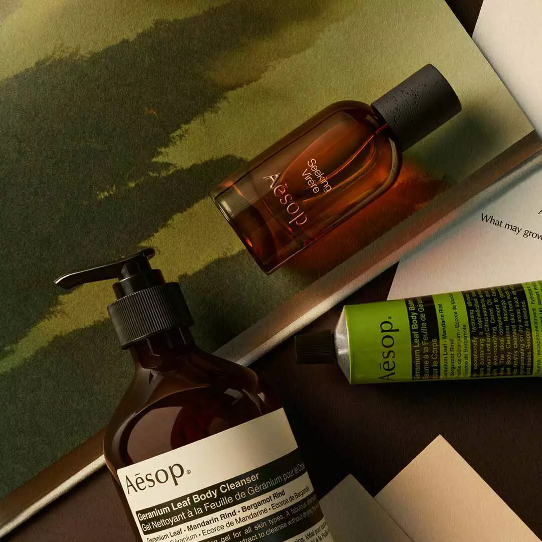 Aesop Seeking Virere bottle with pump bottle and green tube arranged on papers with painted green imagery.