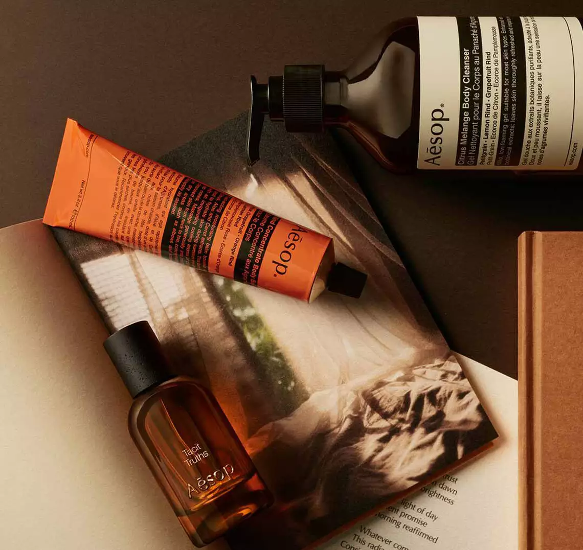 Aesop Tacit Truths fragrance bottle, large amber bottle and cream tube arranged on an open book.