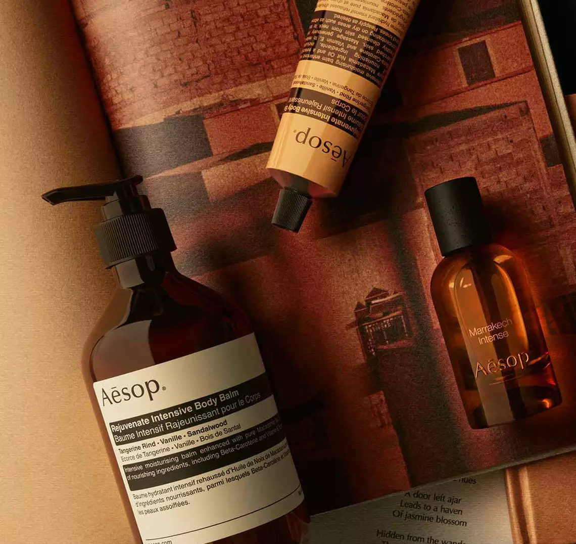 Aesop Marrakech Intense fragrance bottle, large pump bottle and wrapped product on a surface with Moroccan architecture in the background.