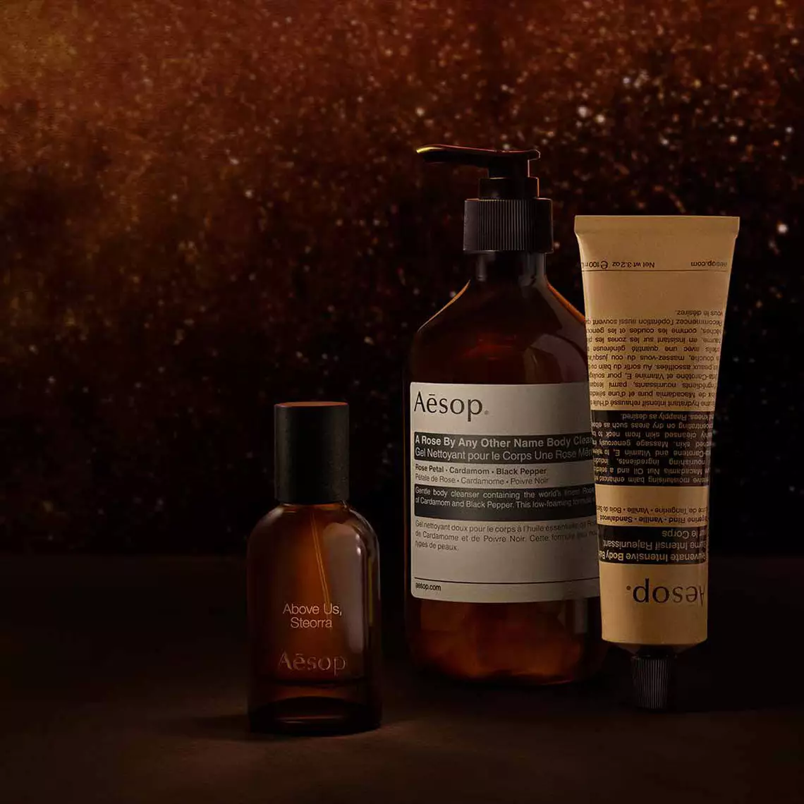 Aesop Above Us, Steorra fragrance bottle, large pump bottle and cosmetic tube arranged on a dark surface.