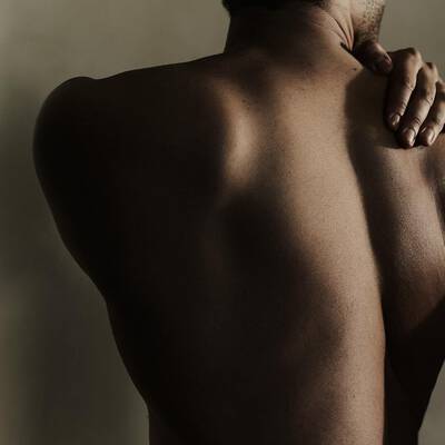 Persons bare back with one hand resting on their shoulder.