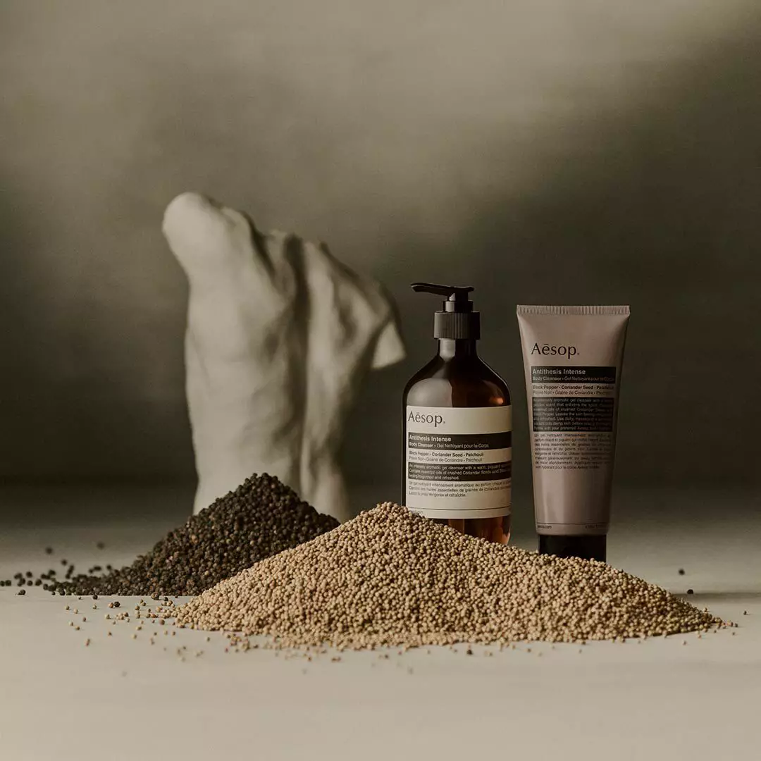 Aesop Antithesis Intense Body Cleanser pump bottle and tube beside piles of black peppercorns and coriander seeds.