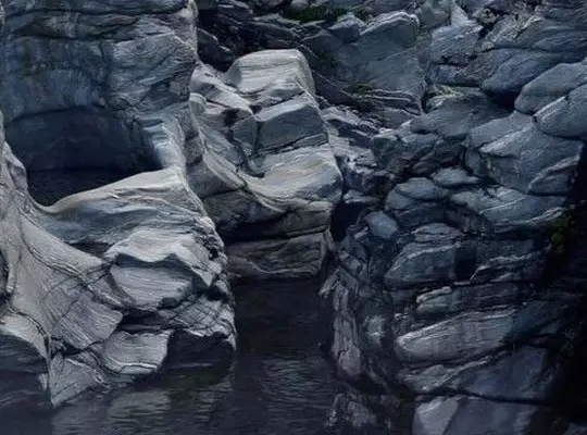 Dark blue-grey rocky gorge with layered sculpted stone formations and a still dark water pool.