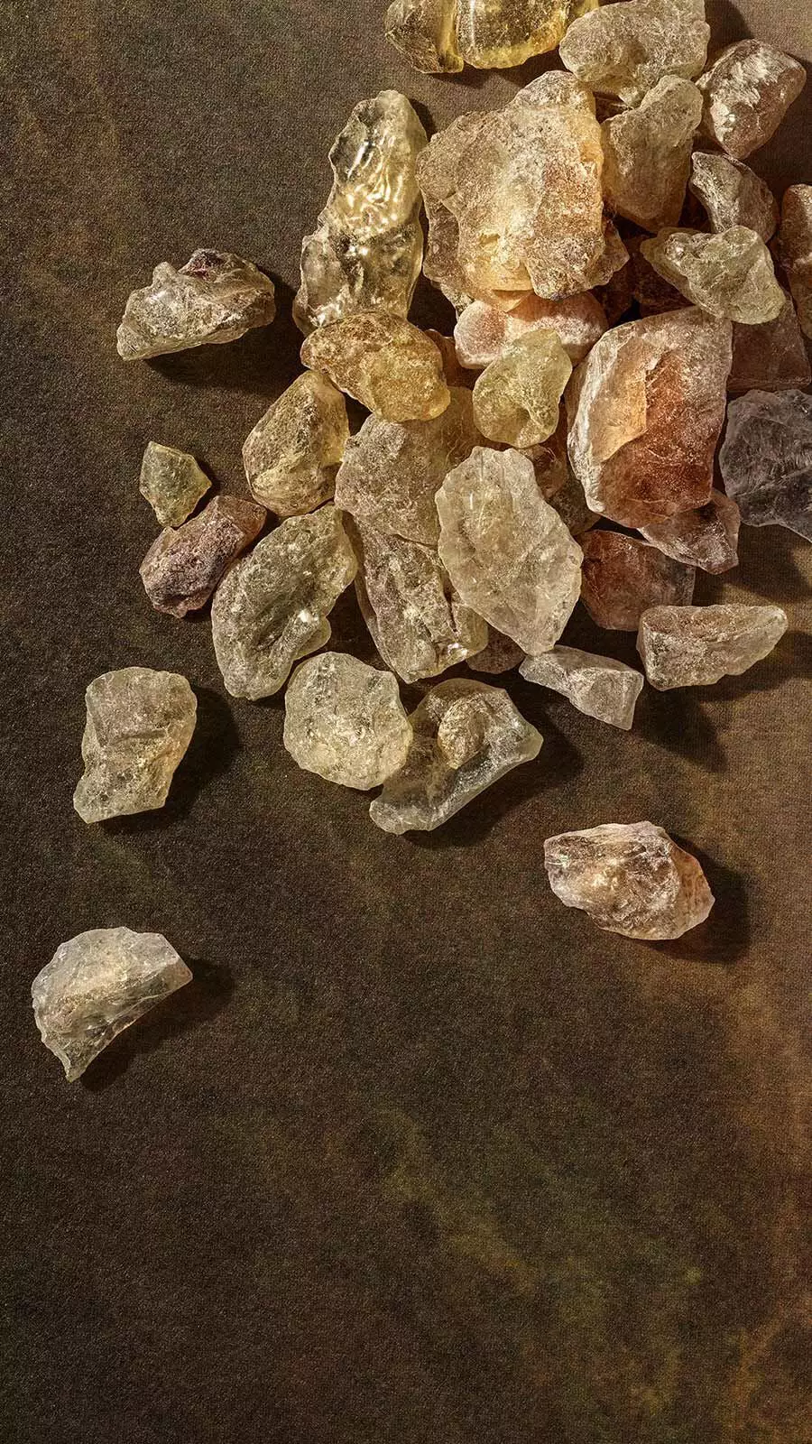 Pale golden frankincense resin crystals in a loose pile on a dark stone surface.