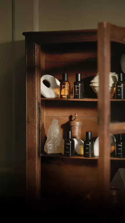 Open wooden cabinet filled with Aesop bottles in warm light.