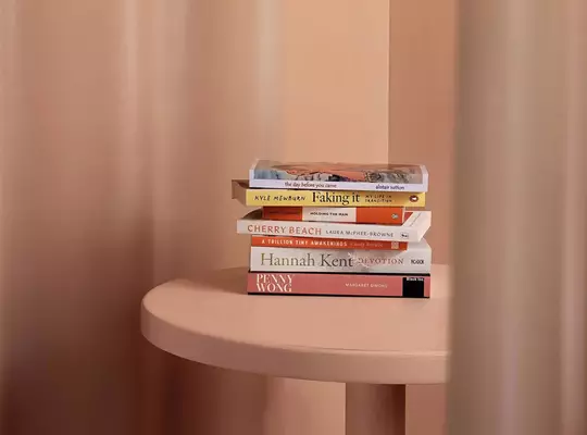Small stack of books on a peach table against a softly draped peach backdrop.