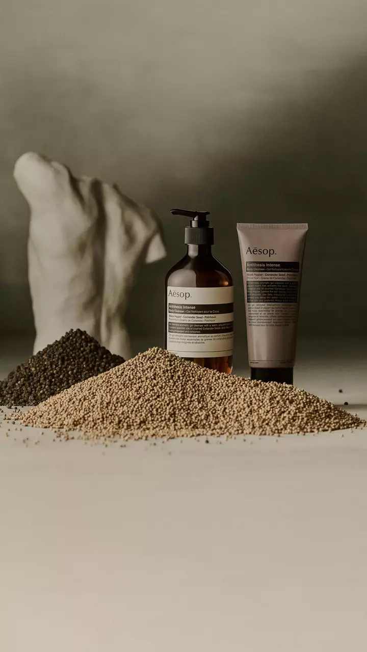 Aesop Antithesis Intense Body Cleanser pump bottle and tube beside piles of black peppercorns and coriander seeds.