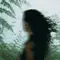 A blurred person in a sleeveless black top, with long dark hair swept sideways, appears against green fern imagery.