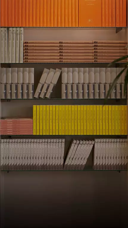 Blurred person walking past warm wooden shelves filled with yellow, orange, and red books.