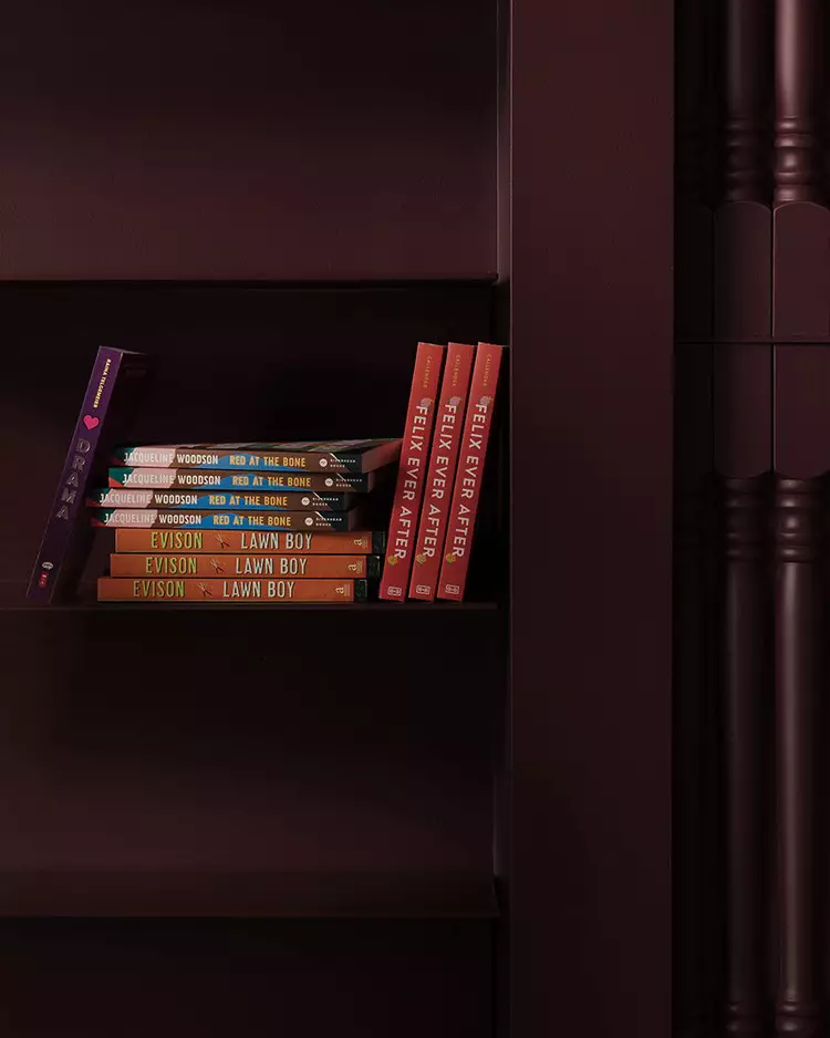 Small row of colourful books on a dark maroon shelf beside ribbed columns.