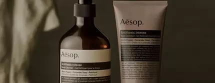 Aesop Antithesis Intense Body Cleanser pump bottle and tube beside piles of black peppercorns and coriander seeds.
