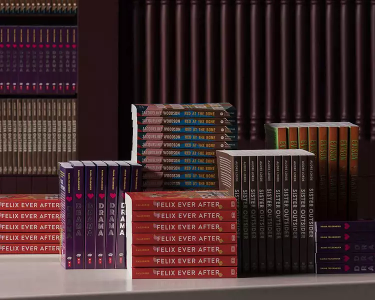 Stacks and rows of colourful books displayed on a pale table before dark ribbed shelves.
