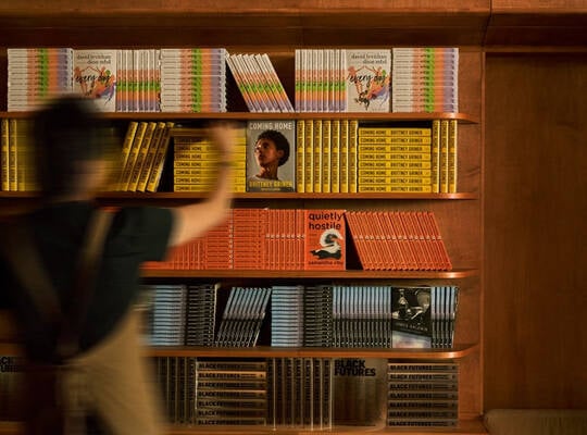 Blurred person walking past warm wooden shelves filled with yellow, orange, and red books.