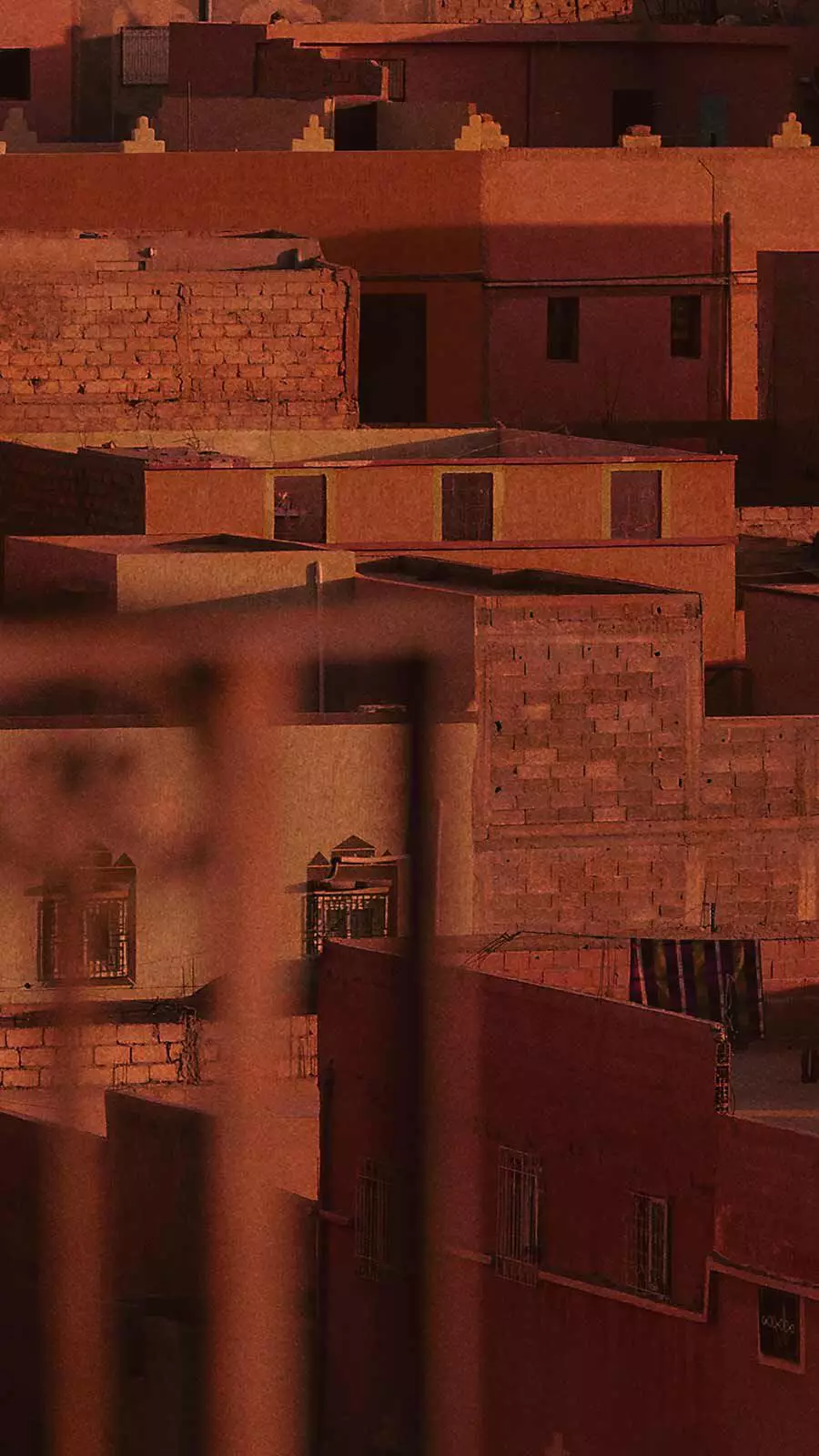 Terracotta-toned Moroccan-style flat-roofed building facades in warm reddish light.