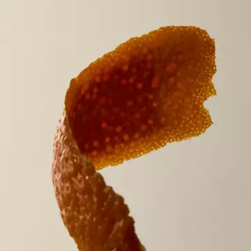 Gros plan d'une ecorce de tangerine enroulee sur fond pale.