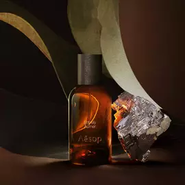 Aesop Entirely Aurner bottle beside a mineral fragment and broad green leaves.