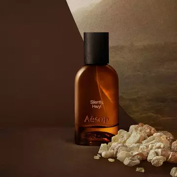 Aesop Silently Hwyl bottle beside resin stones on a dark surface.