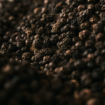 Close-up of black peppercorns scattered across a dark textured surface.
