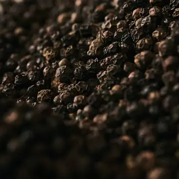Close-up of black peppercorns scattered across a dark textured surface.