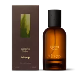Amber glass Aesop Seeking Virere Eau de Parfum bottle beside its brown outer box on a white background.