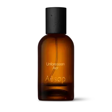 Amber glass Aesop Unforeseen Aer Eau de Parfum bottle with black cap on a white background.