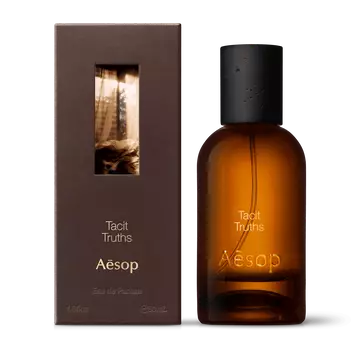 Amber glass Aesop Tacit Truths Eau de Parfum bottle beside its brown outer box on a white background.