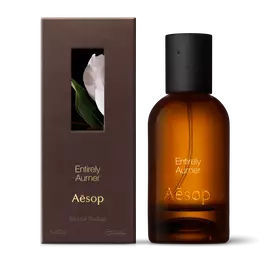 Amber glass Aesop Entirely Aurner Eau de Parfum bottle beside its brown outer box on a white background.