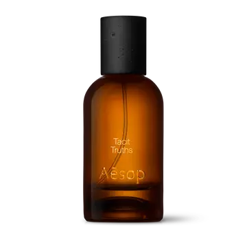 Amber glass Aesop Tacit Truths Eau de Parfum bottle with black cap on a white background.