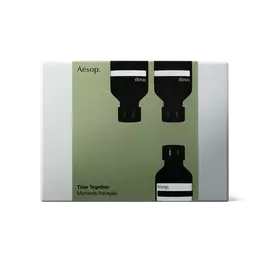 Silver-grey Aesop Time Together gift box with an olive-green sleeve showing two inverted black bottles above one upright bottle.