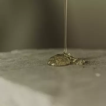 Clear amber gel being poured onto a textured stone surface.