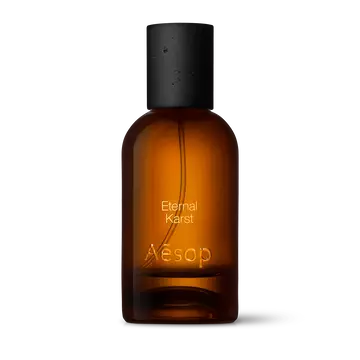 Amber glass Aesop Eternal Karst Eau de Parfum bottle with black cap on a white background.