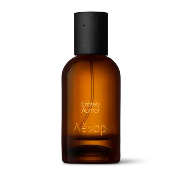 Amber glass Aesop Entirely Aurner Eau de Parfum bottle with black cap on a white background.