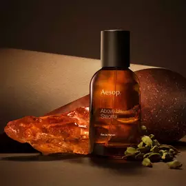 Aesop Above Us, Steorra bottle beside an amber resin piece and green cardamom pods on a warm brown surface.