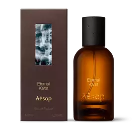 Amber glass Aesop Eternal Karst Eau de Parfum bottle beside its brown outer box on a white background.