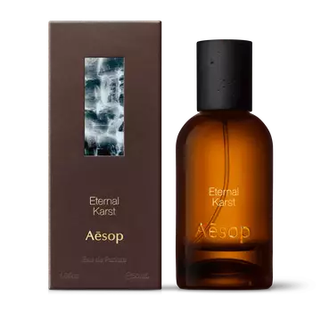 Amber glass Aesop Eternal Karst Eau de Parfum bottle beside its brown outer box on a white background.