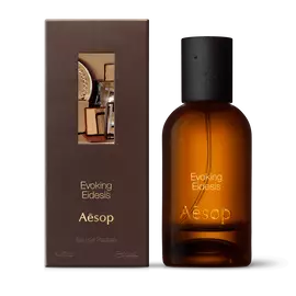 Amber glass Aesop Evoking Eidesis Eau de Parfum bottle beside its brown outer box on a white background.