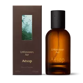 Amber glass Aesop Unforeseen Aer Eau de Parfum bottle beside its brown outer box on a white background.