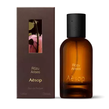 Amber glass Aesop Rozu Arises Eau de Parfum bottle beside its brown outer box on a white background.