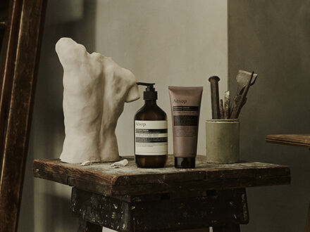 Aesop Antithesis Intense Body Cleanser pump bottle and tube beside piles of black peppercorns and coriander seeds.