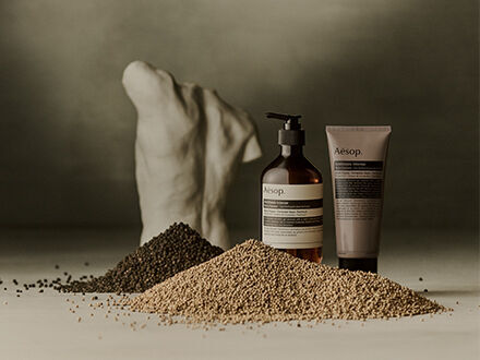 Aesop Antithesis Intense Body Cleanser pump bottle and tube beside a white torso sculpture and brushes on a wooden work table.